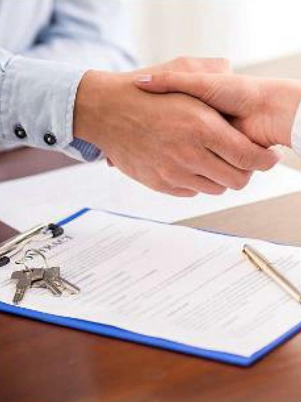 KITAROLL-BATIMENT NOUS ACHETONS Deux mains se serrent au-dessus d'un document et de clés posées sur une table.